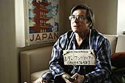 Damit Rudi (Elmar Wepper) in der Millionenstadt Tokio, nicht verloren geht, wird ihm ein Schild mit Adresse um den Hals gehängt (Credit: MAJESTIC & Mathias Bothor)